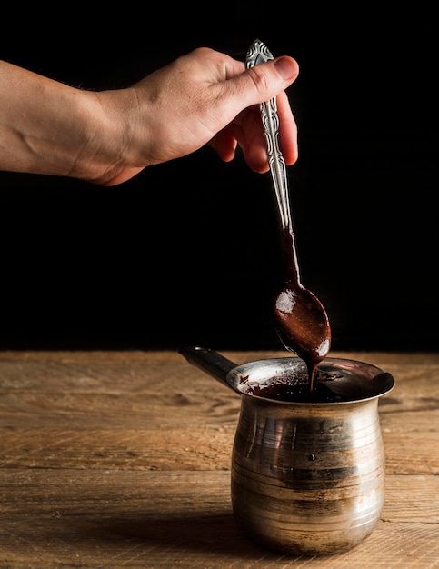 High angle hand holding teaspoon with melted chocolate over pot