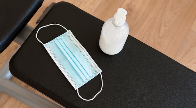 High angle of hand sanitizer and medical mask on gym bench