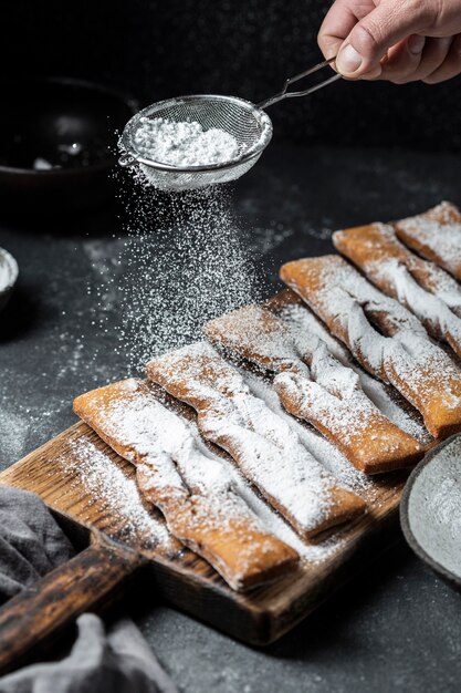 High angle of hand sieving powdered sugar on desserts