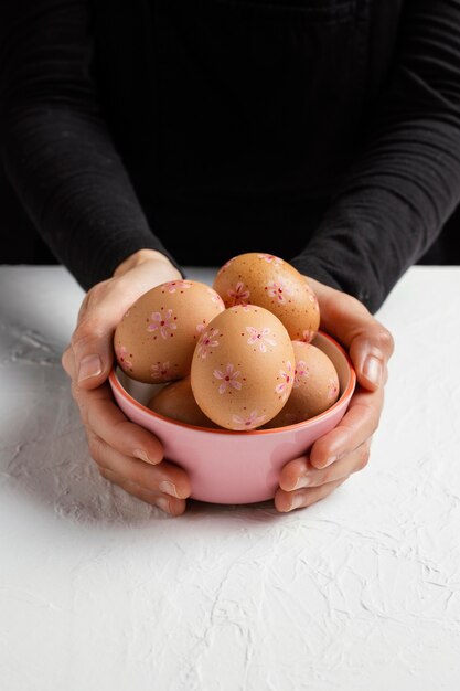 Высокий угол рук, держащих миску с украшенными пасхальными яйцами