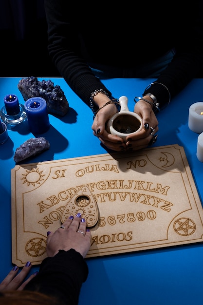 Free photo high angle hands touching ouija board and cup