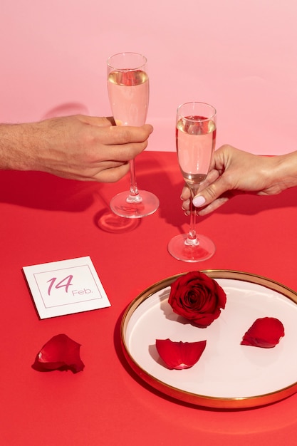 Free photo high angle of hands with glasses cheering for valentines day next to rose on plate