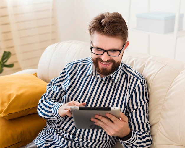 タブレットが付いているソファーで幸せな男の高角