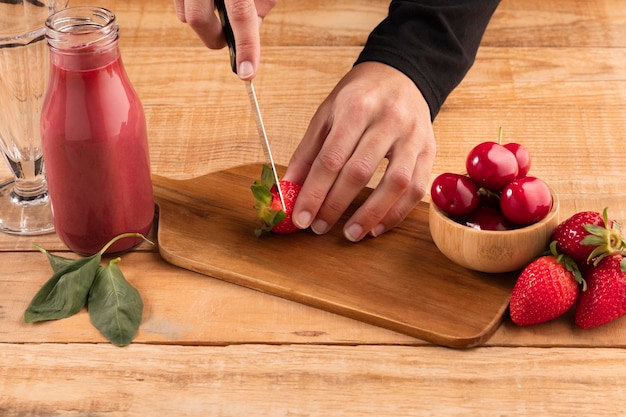 High angle human cutting fruits near smoothies