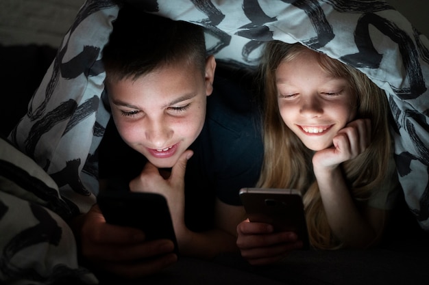 Дети под высоким углом со смартфонами под одеялом