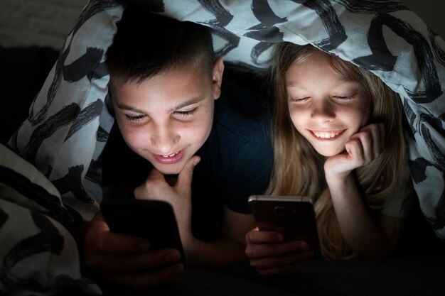 毛布の下でスマートフォンを持つハイアングルの子供たち