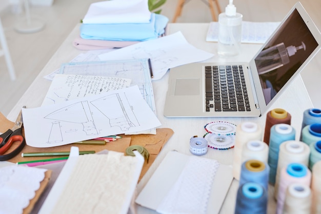 Alto angolo di laptop con piano di linea di abbigliamento e bobine di filo sul tavolo in atelier