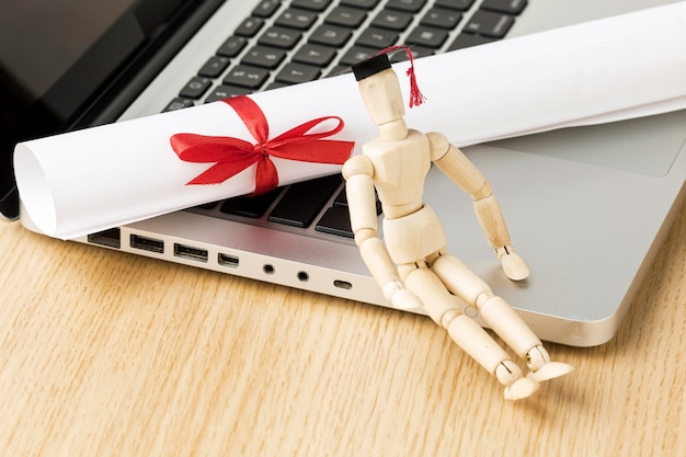 Free photo high angle of laptop with wooden figurine and academic cap