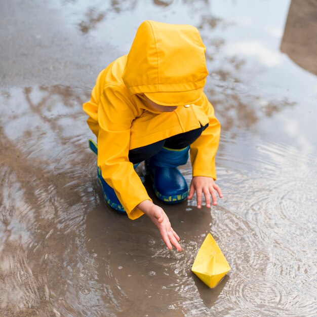 High angle little boy playing with a paper boat