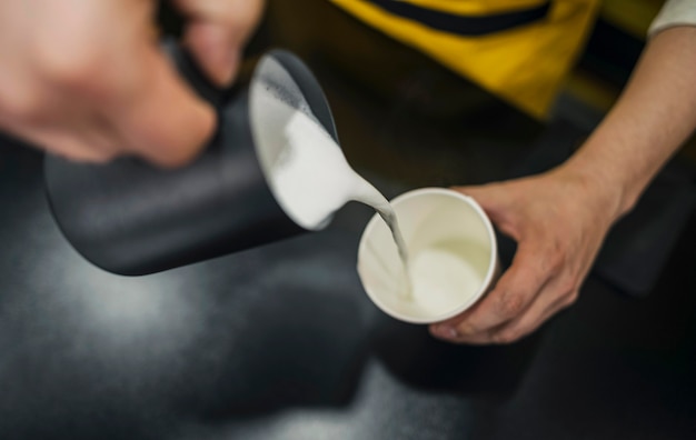 High angle of male barista pouring milk in cup