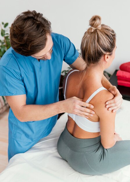 high angle of male osteopathic therapist checking female patient's scapula