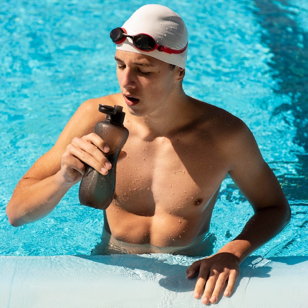 High angle of male swimmer drinking water to stay hydrated