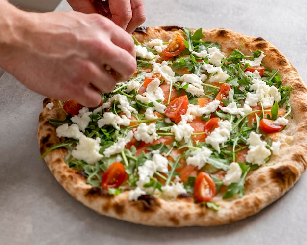 High angle man putting mozzarella on baked pizza dough with smoked salmon slices