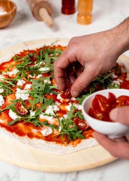 High angle man putting tomatoes on pizza