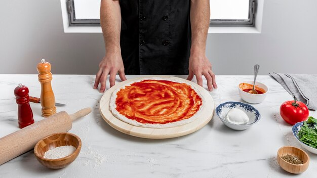 Человек под высоким углом намазывает томатный соус на тесто для пиццы