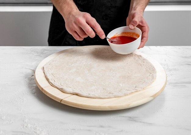 High angle man spreading tomato sauce on pizza dough