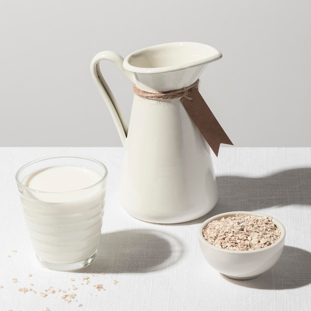 Foto gratuita alto angolo di bicchiere di latte con brocca e ciotola di farina d'avena