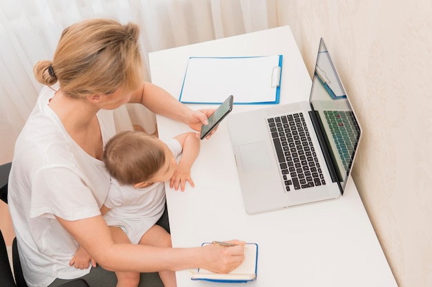 Free photo high angle mother holding baby sitting at desk