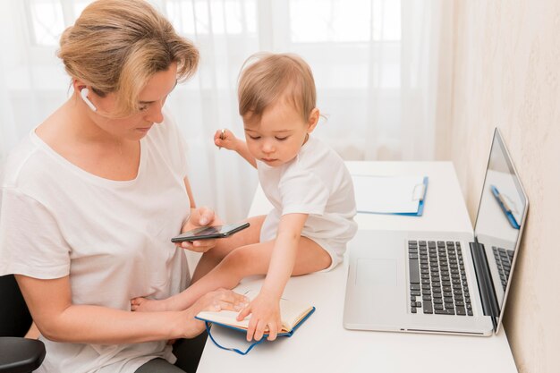 High angle mother looking at phone and baby on desk