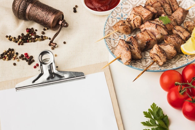 High angle of notepad with plate of delicious kebab and condiment grinder