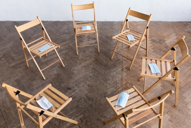 Бесплатное фото Высокий угол пустых стульев с медицинскими масками, подготовленными для сеанса групповой терапии