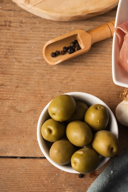 Free photo high angle olives and black peppers on cutting board