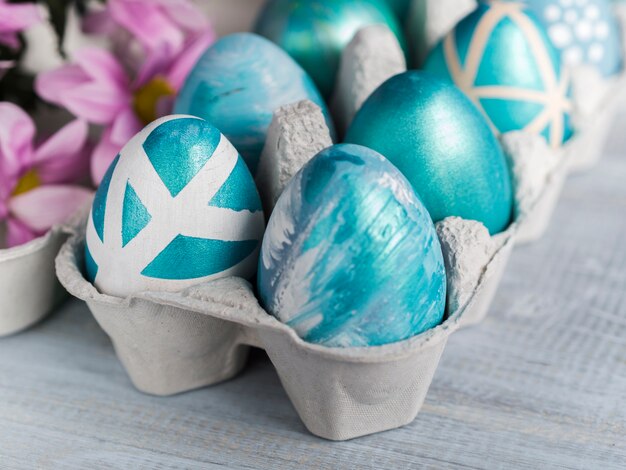 High angle of painted easter eggs in carton with flowers