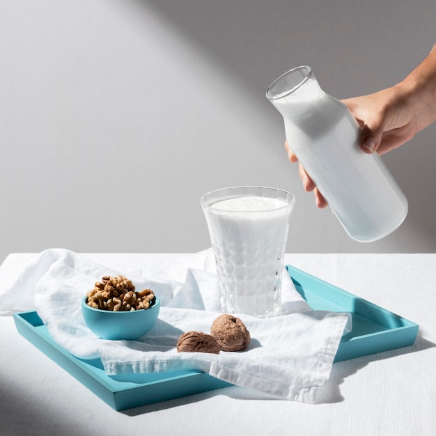 High angle of person pouring milk in full glass with walnuts on tray