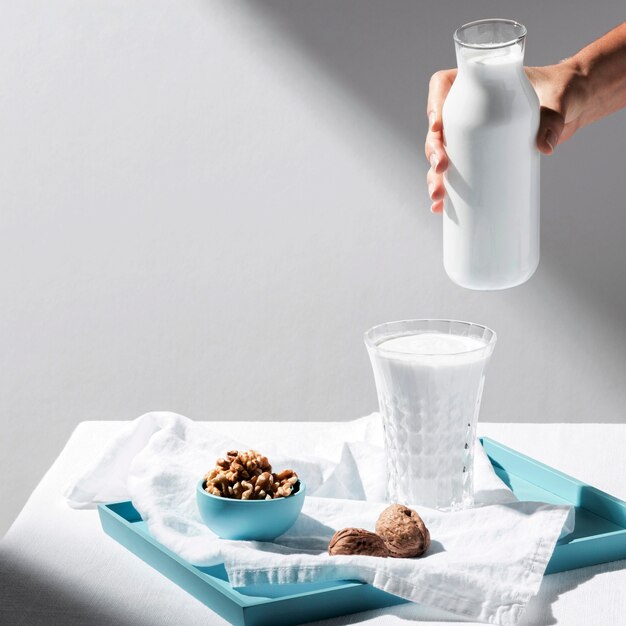 High angle of person pouring milk in glass with walnuts on tray