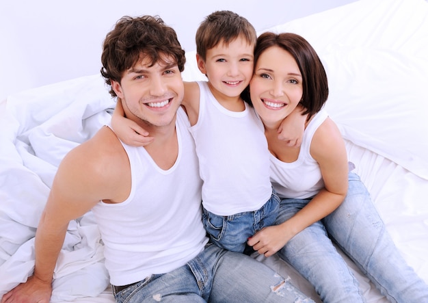 High angle portrait of the Happy parents with little child sitting on a bed