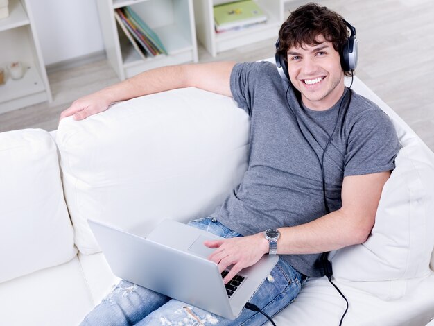 High angle portrait of smiling young handsome guy with laptop using headset
