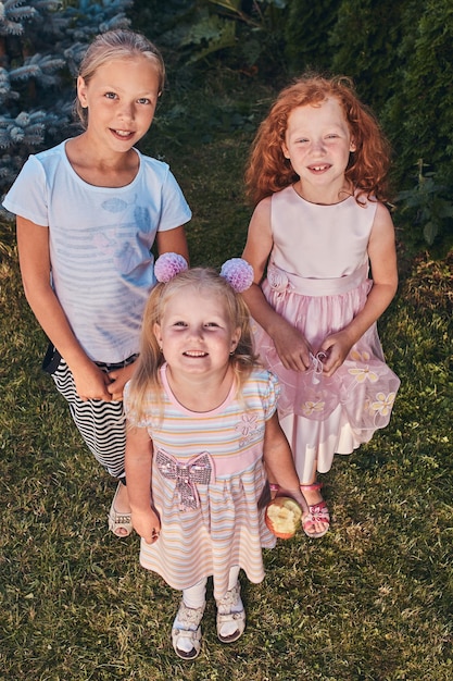 Foto gratuita ritratto ad alto angolo di tre piccole amiche felici in piedi su un prato nel parco.