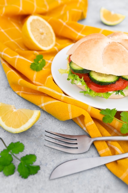 Высокий угол сэндвич на тарелку со столовыми приборами и дольками лимона