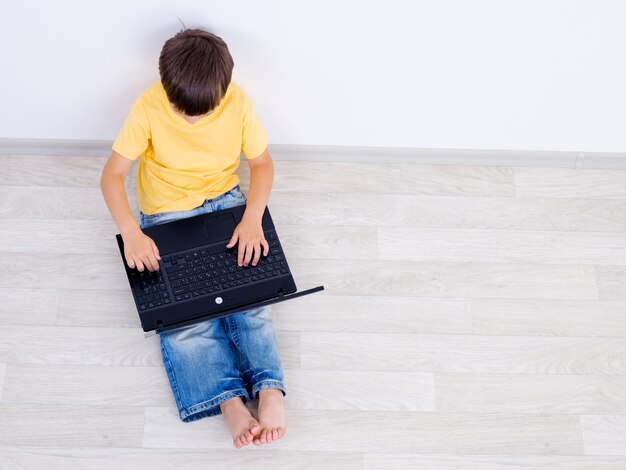 Foto gratuita tiro ad alto angolo del ragazzino utilizzando laptop - al chiuso