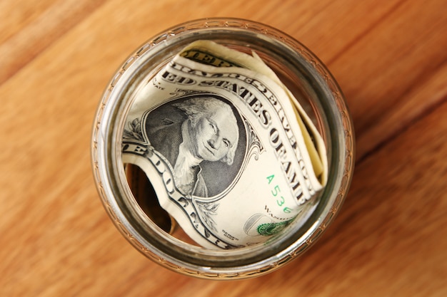 High angle shot of American dollar bills in a glass jar on a wooden surface