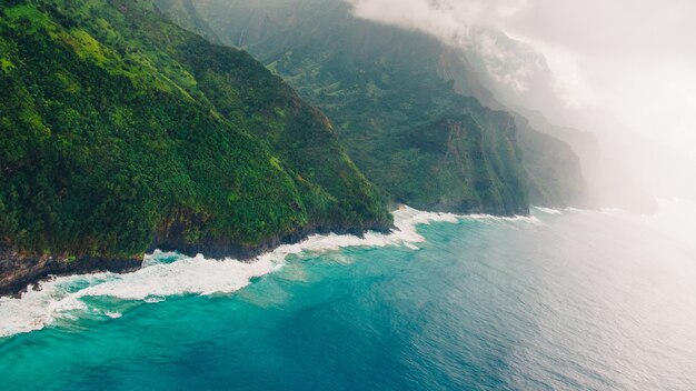 High angle shot of the beautiful foggy cliffs over the calm blue ocean captured in Kauai, Hawaii