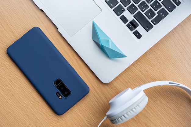 High angle shot of a blue cellphone, headphones, a laptop, and an origami on a wooden surface