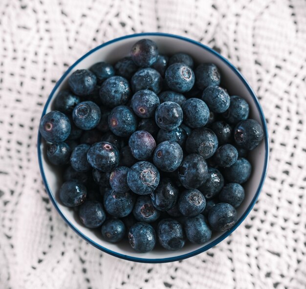 High angle shot of a bowl filled with blueberries on a nice white tablecloth on a table