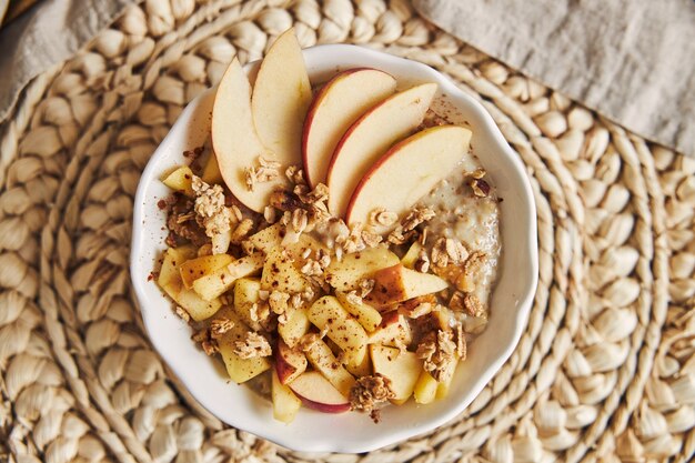 High angle shot of a bowl Porridge with cereal and nuts, and slices of apple on a wooden table