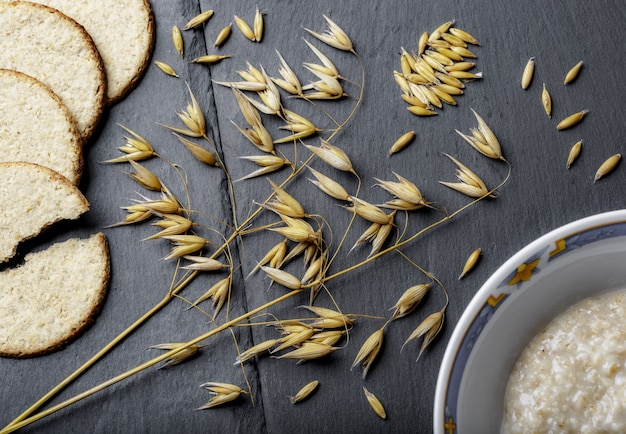 High angle shot of branches of wheat, fresh bread, and porridge on a grey surface