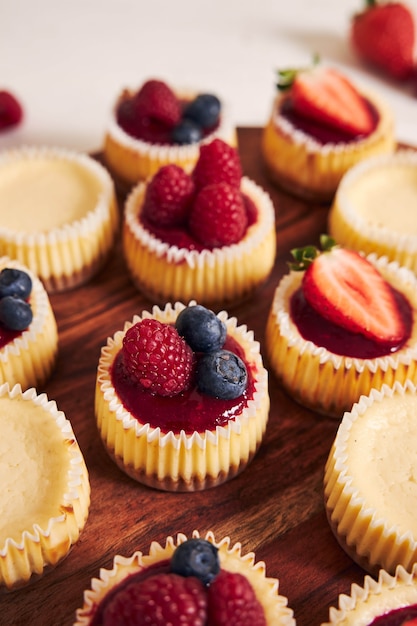 High angle shot of cheese cupcakes with fruit jelly and fruits on a wooden plate