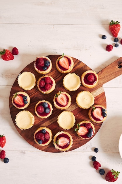 High angle shot of cheese cupcakes with fruit jelly and fruits on a wooden plate