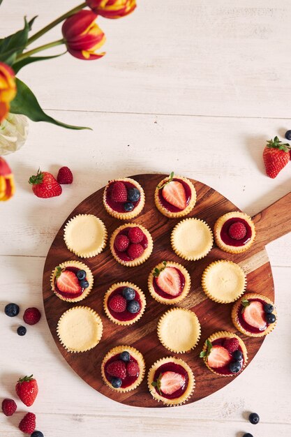 High angle shot of cheese cupcakes with fruit jelly and fruits on a wooden plate