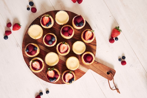 High angle shot of cheese cupcakes with fruit jelly and fruits on a wooden plate