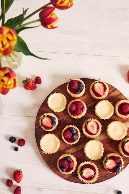 High angle shot of cheese cupcakes with fruit jelly and fruits on a wooden plate