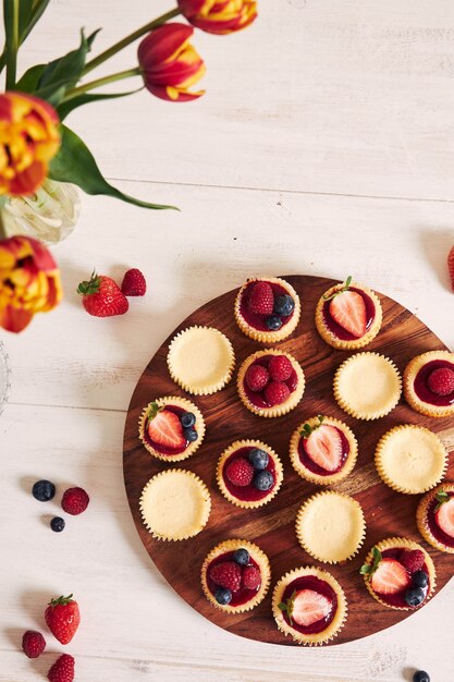 High angle shot of cheese cupcakes with fruit jelly and fruits on a wooden plate