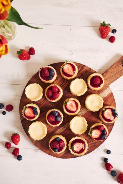 High angle shot of cheese cupcakes with fruit jelly and fruits on a wooden plate