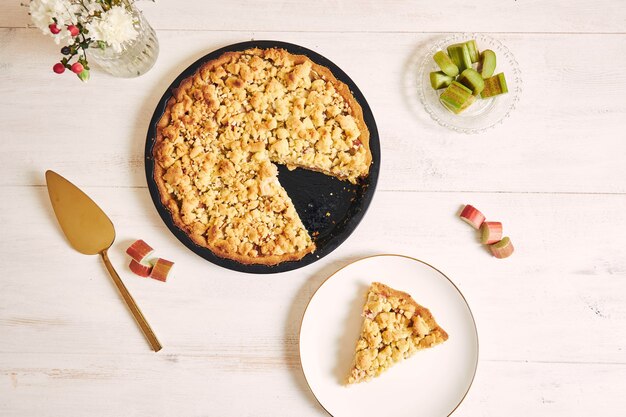 High angle shot of a crispy Rhabarbar cake tart and a slice on plate on white table