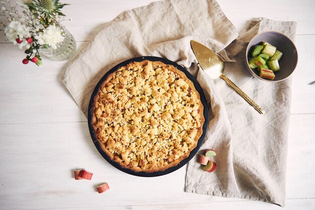 High angle shot of a crispy Rhabarbar cake tart and some ingredients on a white table