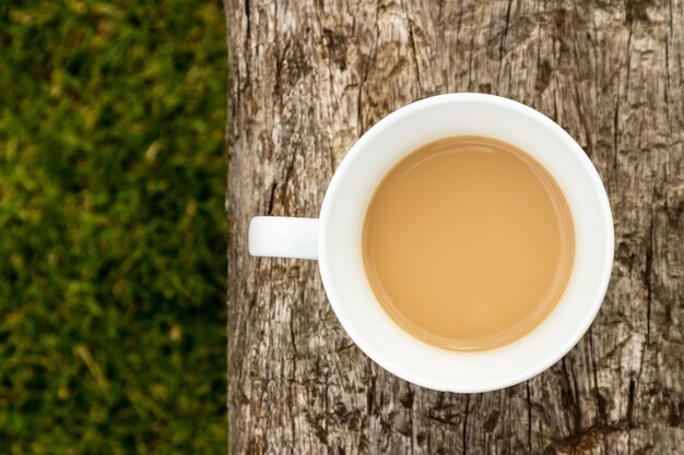 High angle shot of a cup of coffee on a wooden surface over the grass covered field